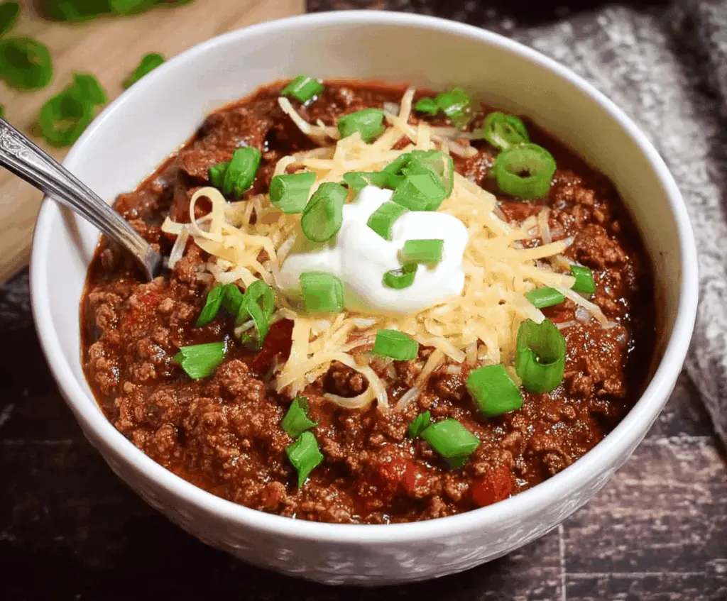 A bowl of hearty low-carb chili topped with shredded cheese and fresh cilantro, served with side vegetables, highlighting a healthy, low-carb meal option.
