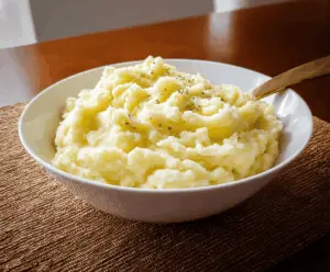 Creamy homemade mashed potatoes topped with a pat of butter and fresh herbs, served in a rustic bowl, perfect for a comforting meal.