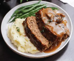 Delicious homemade meatloaf topped with rich brown gravy served on a plate with mashed potatoes and vegetables