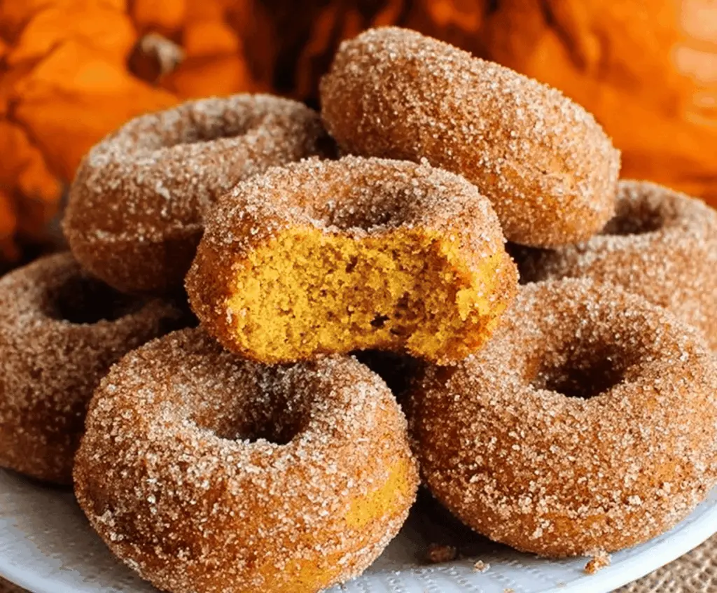 Freshly baked pumpkin donuts glazed with cinnamon sugar on a rustic plate, perfect for fall desserts.