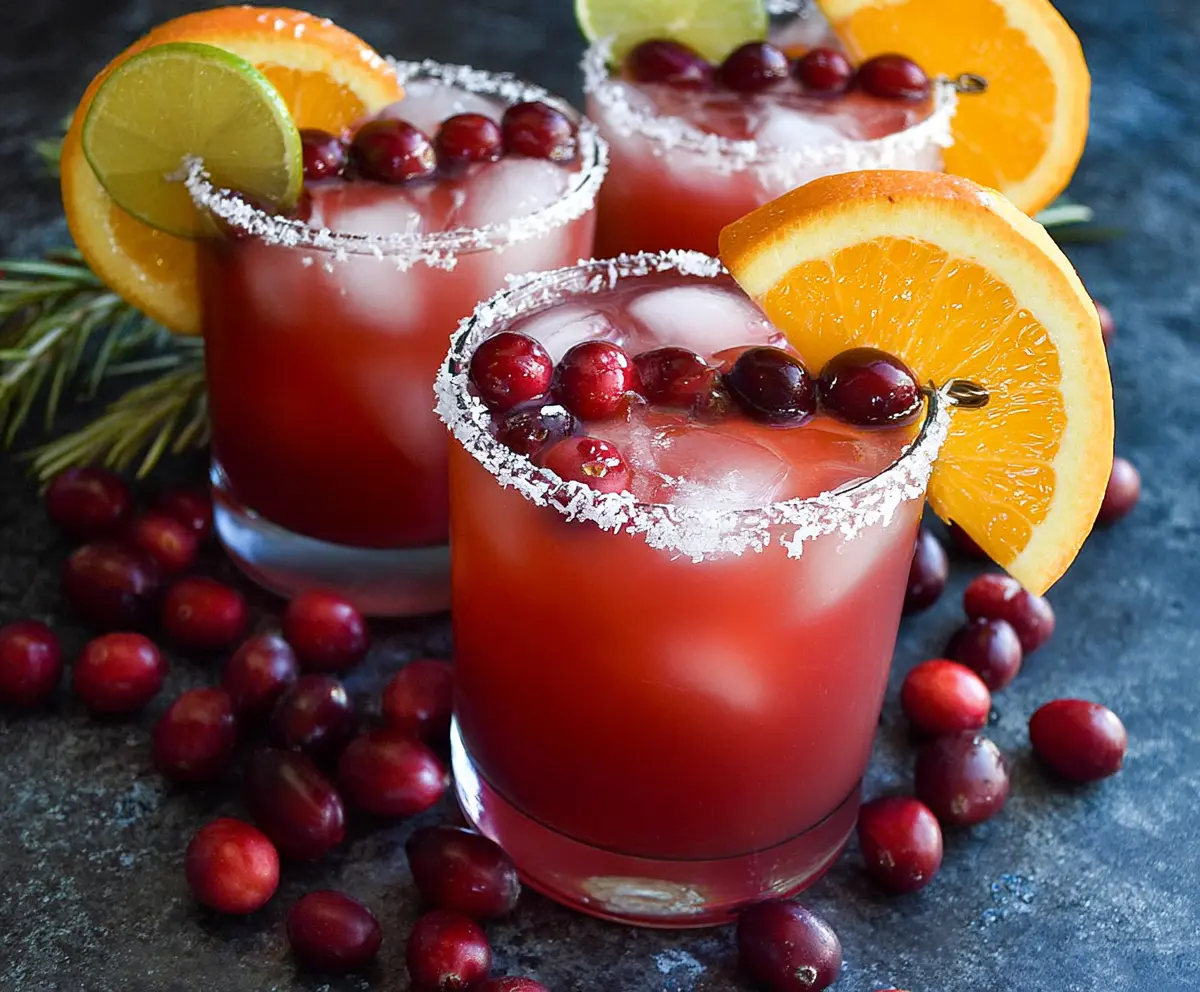 Refreshing cranberry orange margarita cocktail in a glass with fresh cranberries and orange slices.