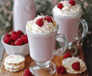 Creamy Raspberry White Hot Chocolate in a mug topped with whipped cream and fresh raspberries