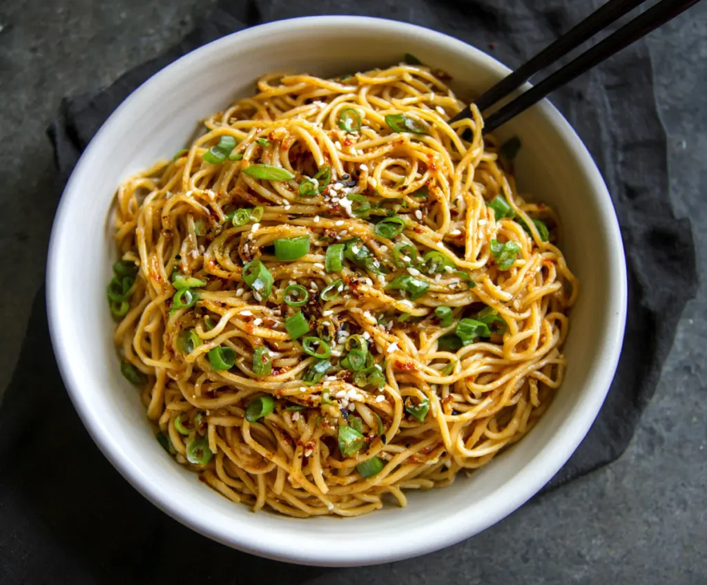 Savory Asian Garlic Noodles garnished with chopped green onions on a plate.
