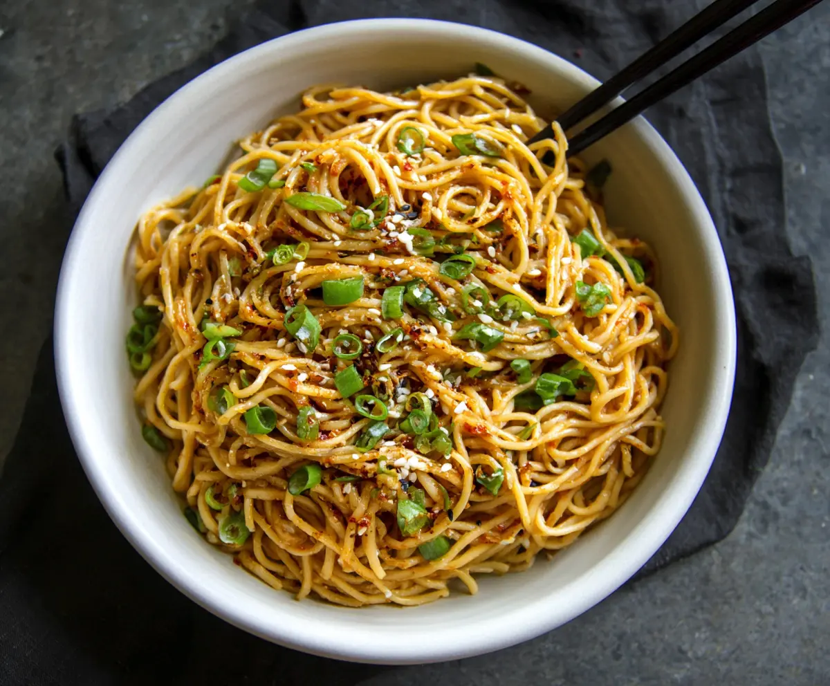 Savory Asian Garlic Noodles garnished with chopped green onions on a plate.