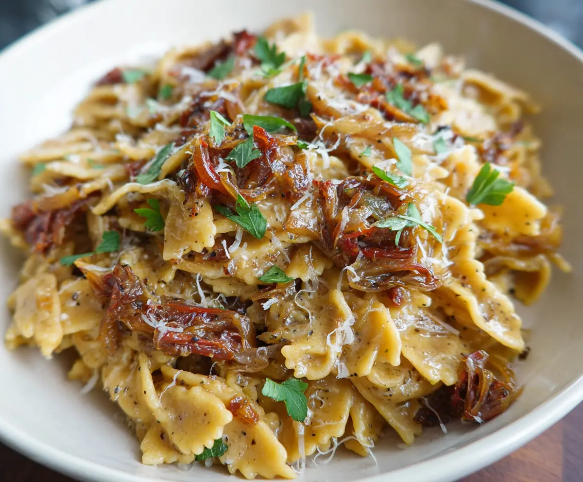 Delicious caramelized onion pasta garnished with herbs on a plate.