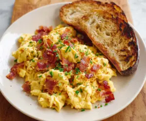 Delicious cheesy scrambled eggs with crispy bacon on a breakfast plate.