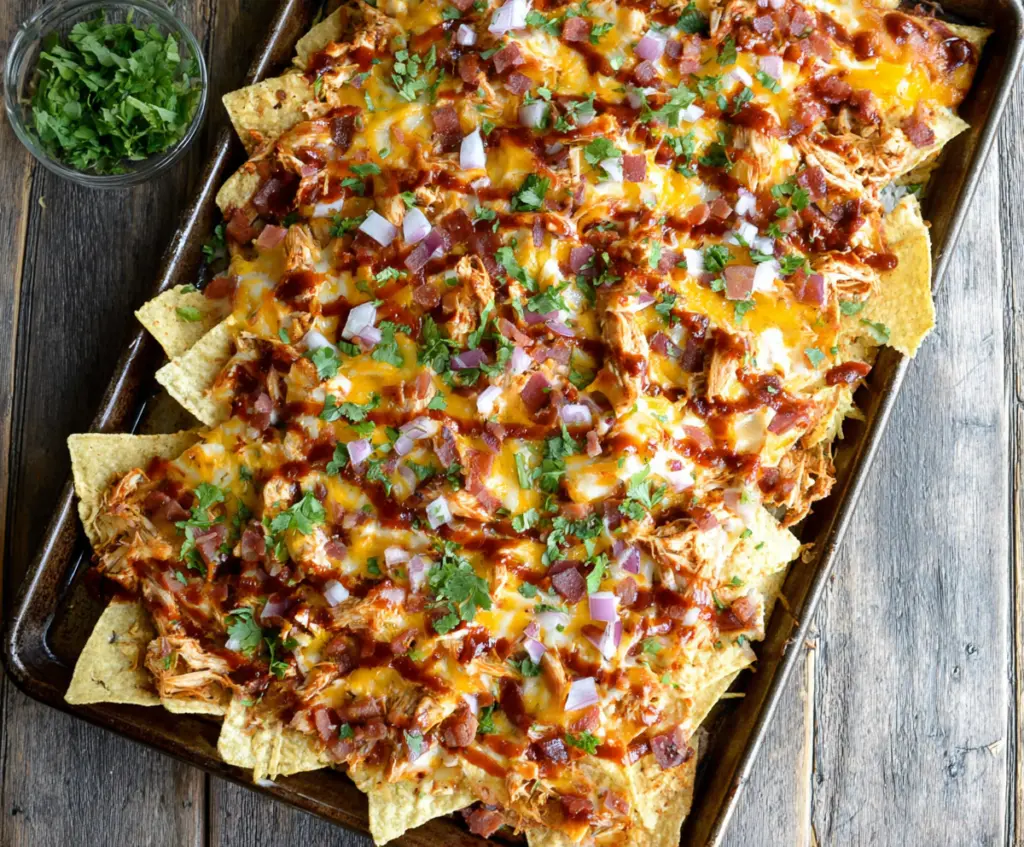Sheet Pan BBQ Chicken Nachos topped with melted cheese and fresh toppings, perfect for game day snacking.