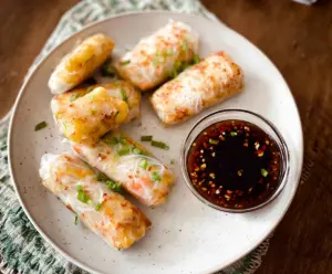 Crispy air fryer rice paper rolls filled with fresh vegetables and herbs on a white plate.