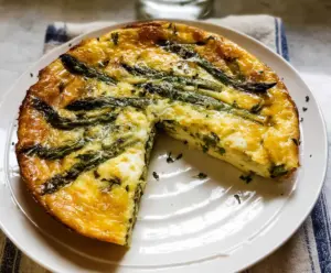 Delicious crustless asparagus quiche garnished with fresh herbs on a white plate.